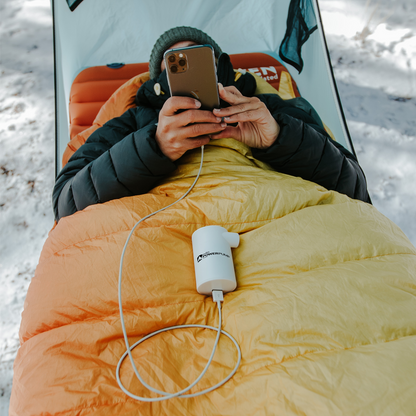 Man using his phone that's charging with a portable sleeping pad air pump